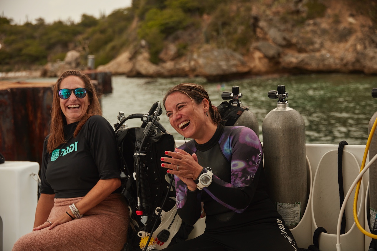 two women divers laugh on the boat before going diving after being told about the marine life identifier mask attachment