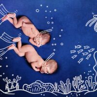 Nude Baby Twins scuba diving using snorkel. Two newborns dive to the incredible undersea to see corals, many fishes, crabs, squids, star fish, shells and jellyfish. Deep blue background.