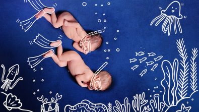 Nude Baby Twins scuba diving using snorkel. Two newborns dive to the incredible undersea to see corals, many fishes, crabs, squids, star fish, shells and jellyfish. Deep blue background.