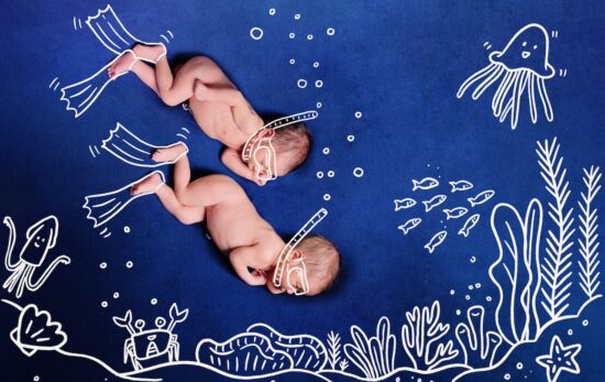 Nude Baby Twins scuba diving using snorkel. Two newborns dive to the incredible undersea to see corals, many fishes, crabs, squids, star fish, shells and jellyfish. Deep blue background.