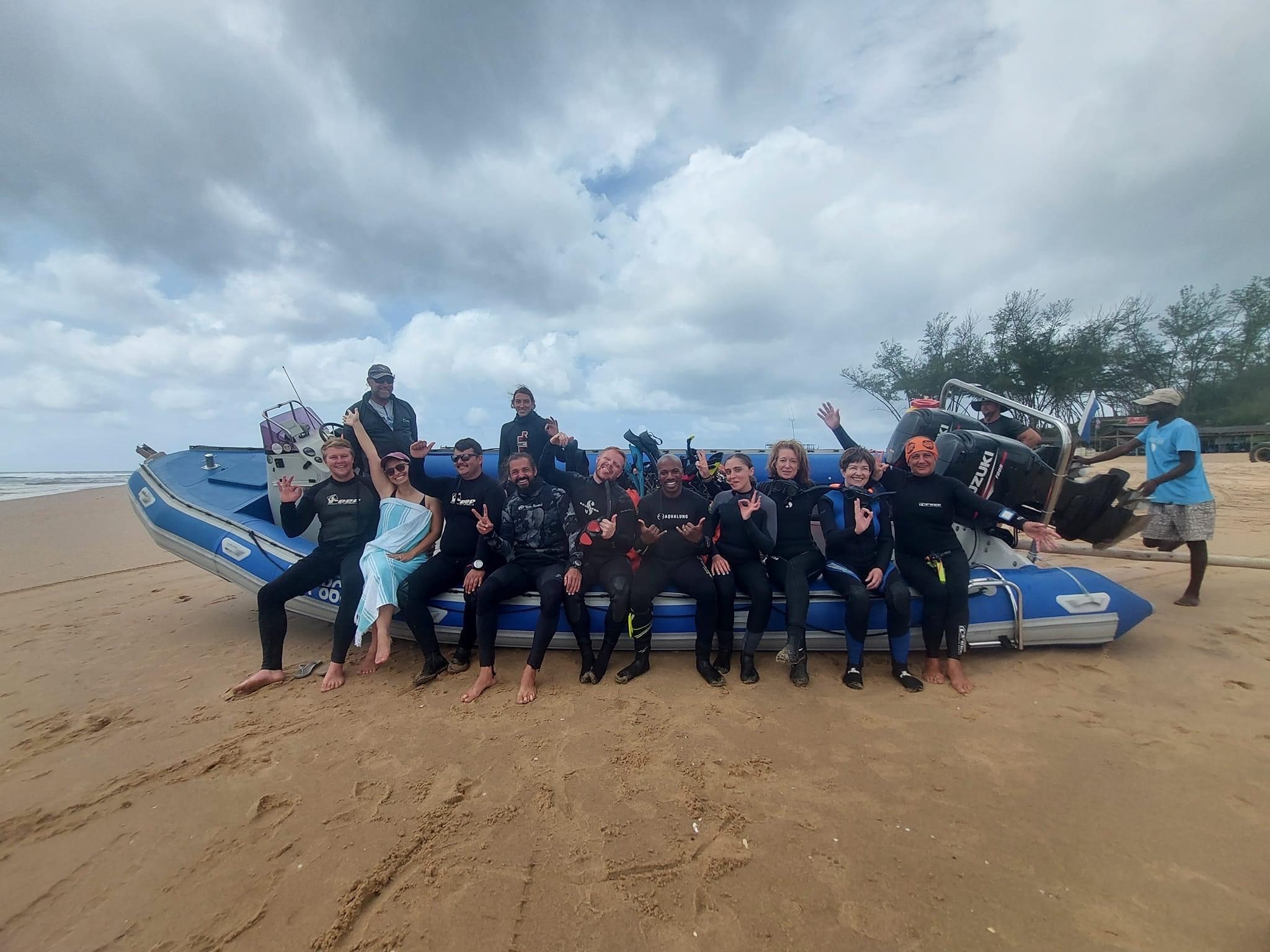Group photo of divers on the beach sitting on a diving boat. They pose excitedly for the camera after a scuba dive.
