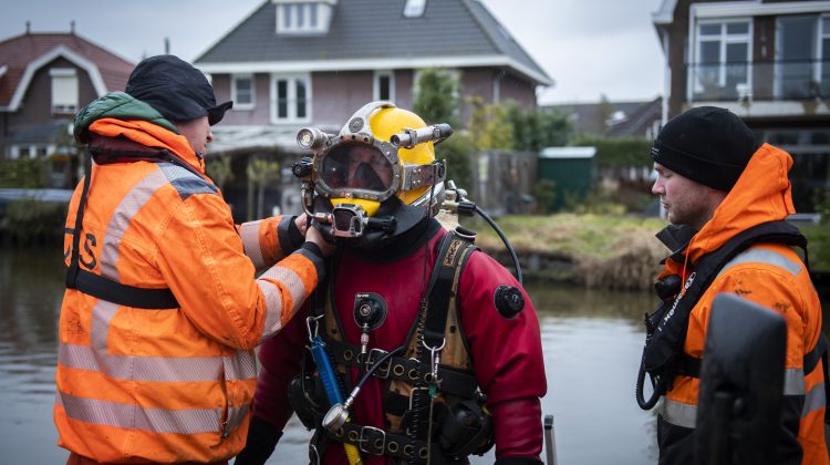A commercial diver and explosives remover enters the water in a dive suit.