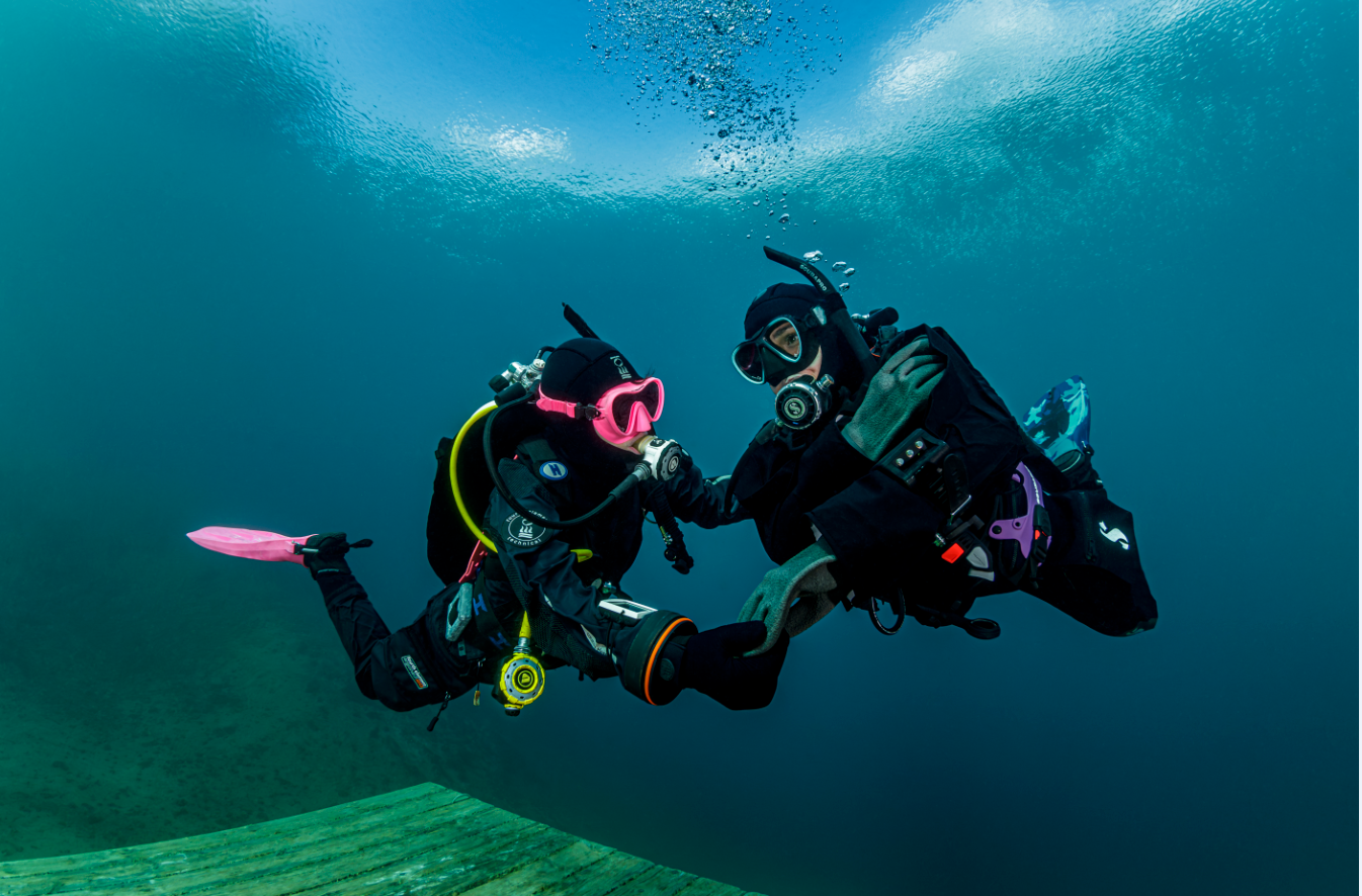 two scuba divers hold hands underwater