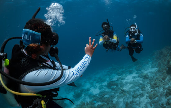 a padi divemaster signals okay to two other divers on a fun dive in the Maldives