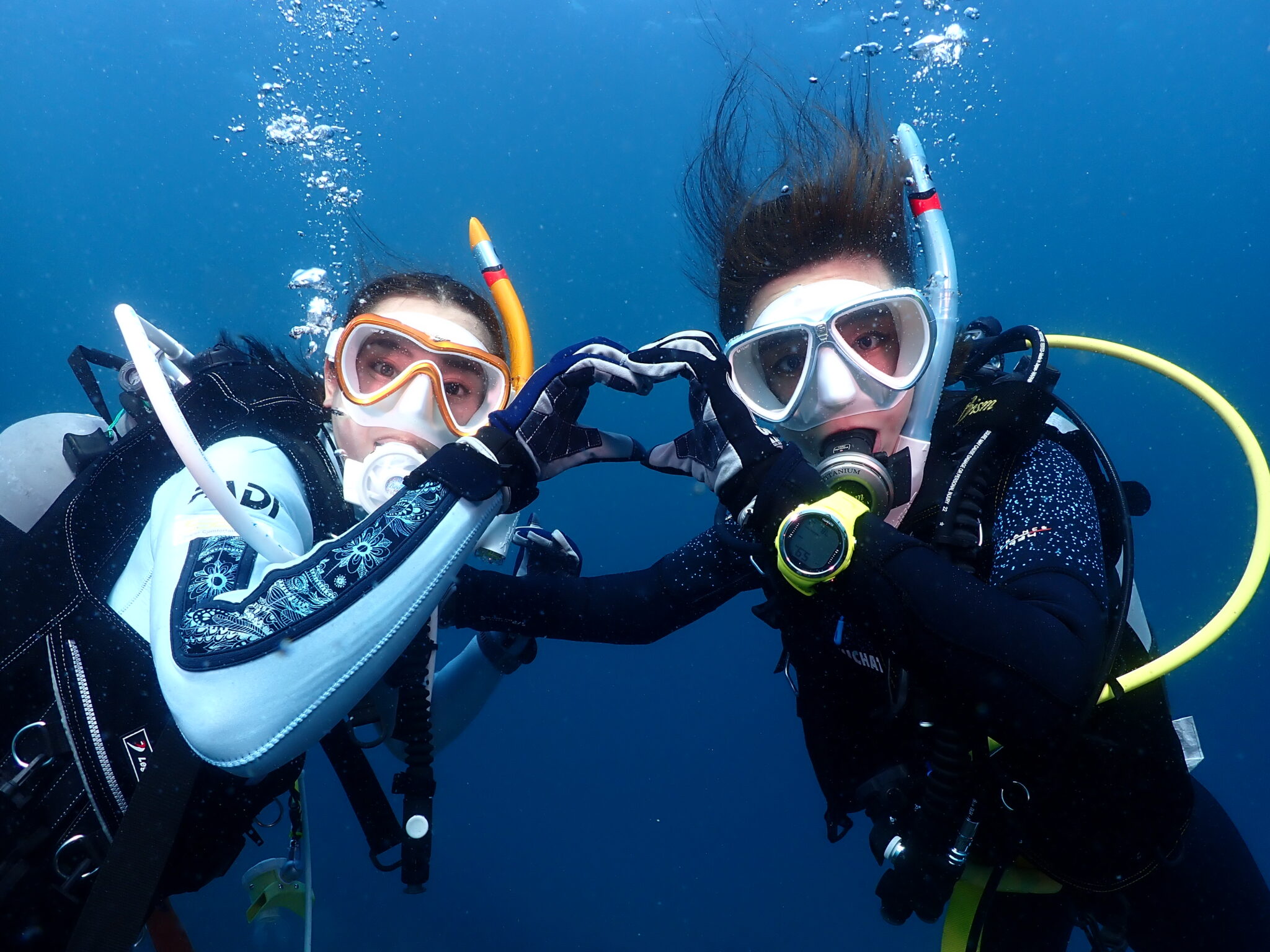 two female divers making a herat with thier hands underwater