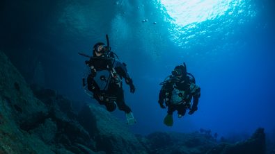 two divers swim in dry suits in New Zealand underwater