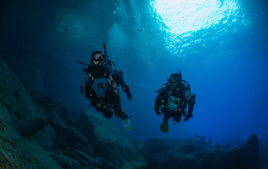 two divers swim in dry suits in New Zealand underwater