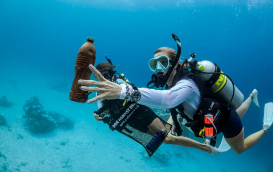 A diver picks up a bottle in the ocean while scuba diving