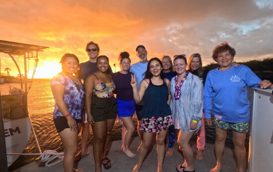 a group of people hang out on a boat in Hawaii at sunset