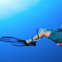A scuba diver swimming in the blue with a diving knife strapped to his leg