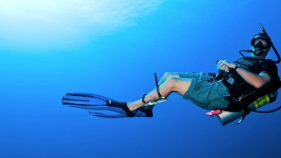 A scuba diver swimming in the blue with a diving knife strapped to his leg