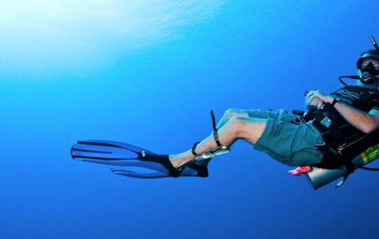 A scuba diver swimming in the blue with a diving knife strapped to his leg