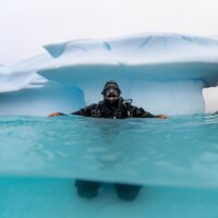 A diver floats at the surface near an iceberg in Antarctica.