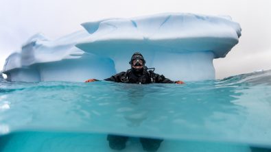 A diver floats at the surface near an iceberg in Antarctica.