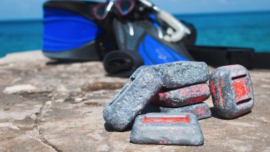 Scuba diving weights on rock by the ocean with equipment in background