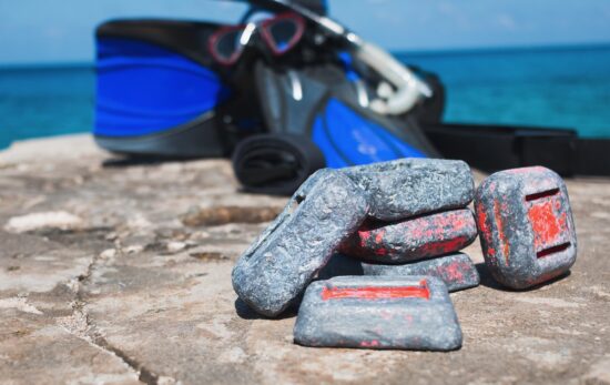 Scuba diving weights on rock by the ocean with equipment in background