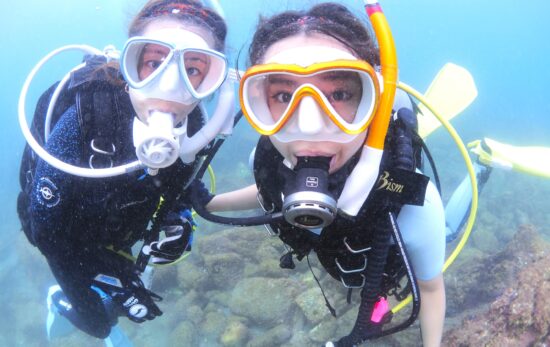 Two female divers shoulder to shoulder in the water, looking at the camera.