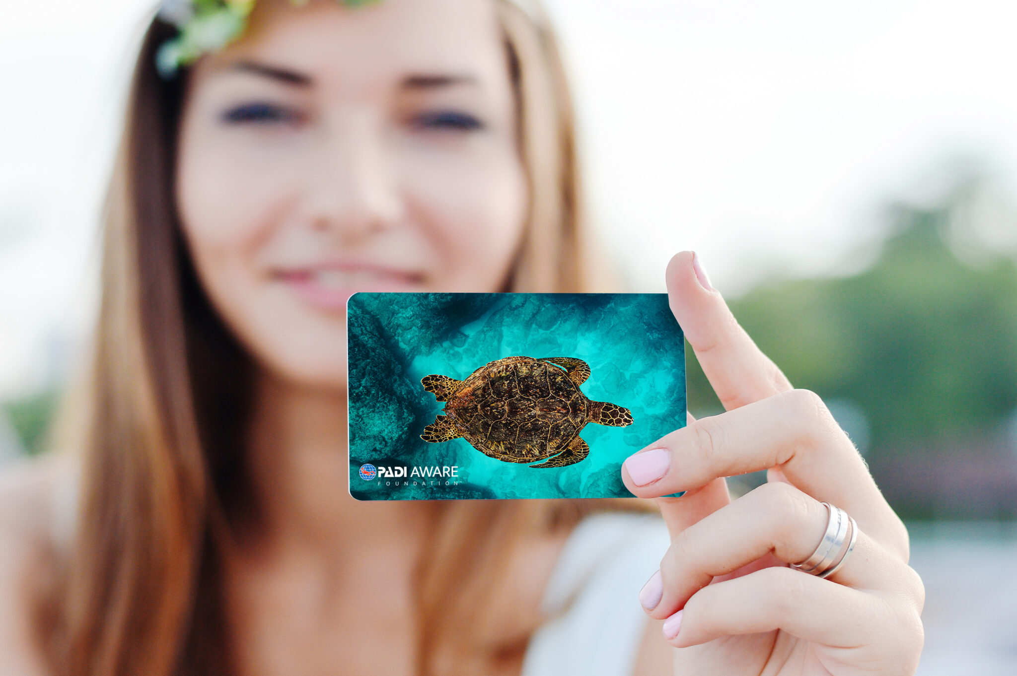 A female diver holding up a PADI AWARE certification card featuring a sea turtle design, one of the best conservation gifts