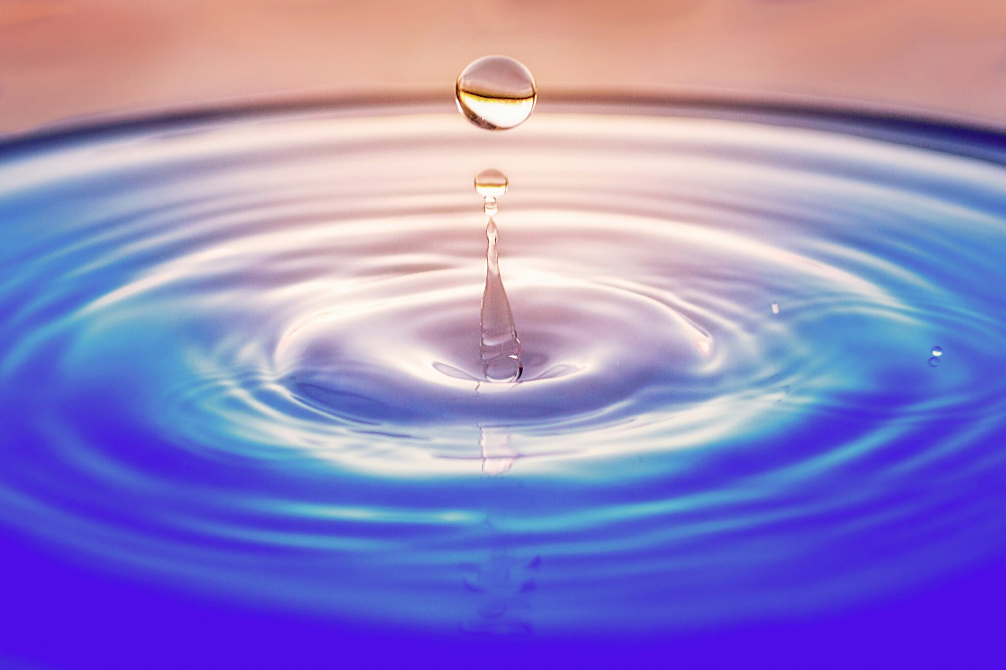 A close-up photo of a perfectly round water droplet splashing and causing a ripple, an example of what is unique about water