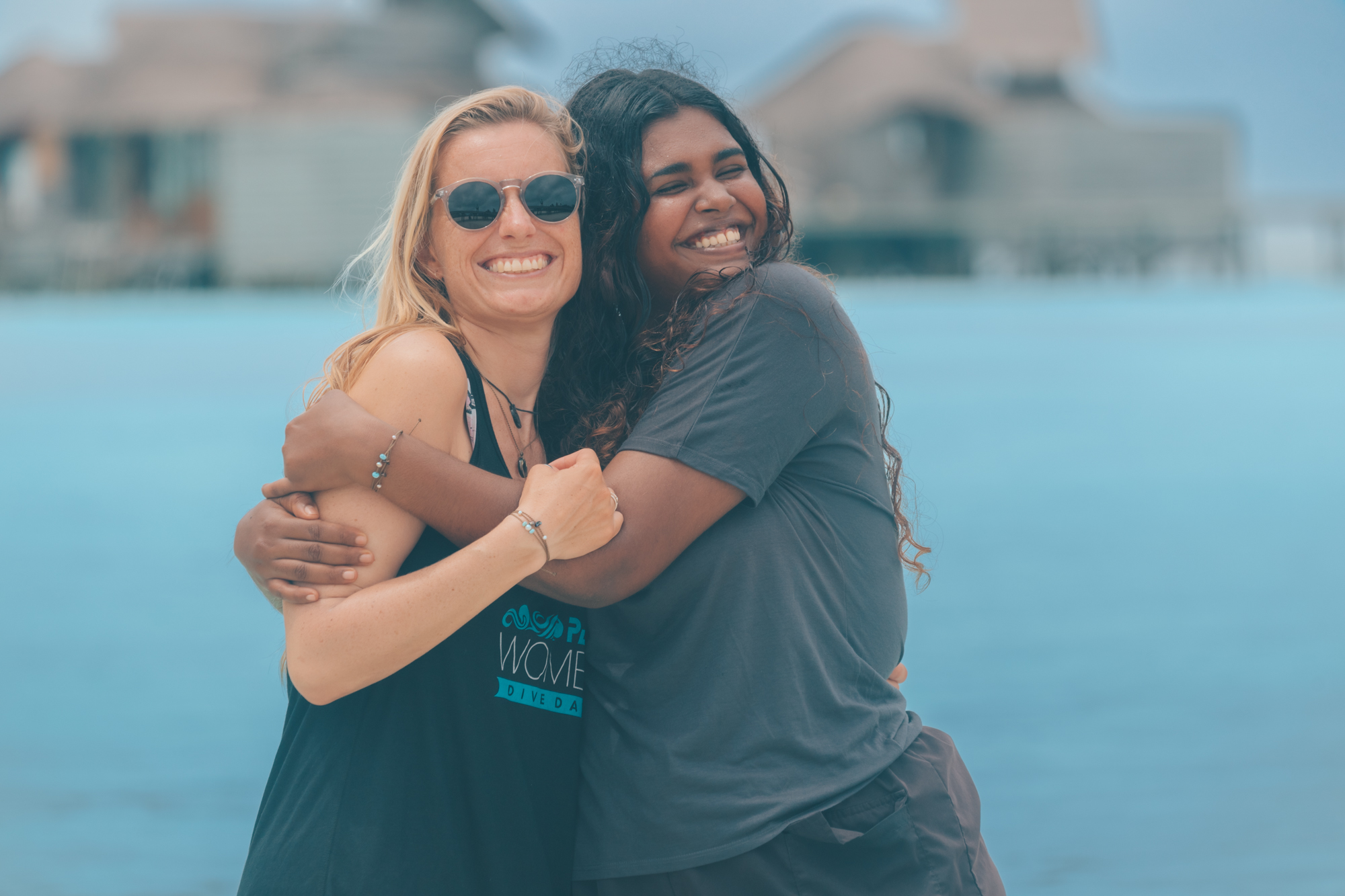 two women smile for the camera while hugging each other on a beach in the Maldives