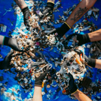 eight hands holding small pieces of plastic retrieved from the ocean