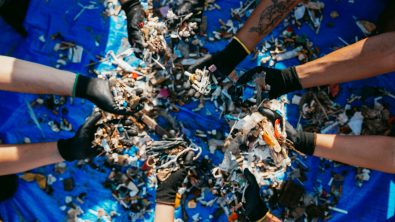 eight hands holding small pieces of plastic retrieved from the ocean