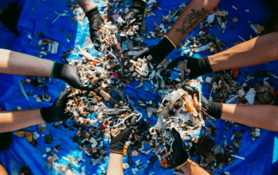 eight hands holding small pieces of plastic retrieved from the ocean