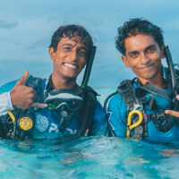 two divers pose and smile for the camera on the surface of the water