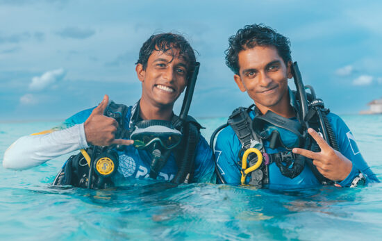 two divers pose and smile for the camera on the surface of the water