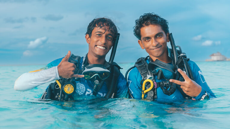 two divers pose and smile for the camera on the surface of the water