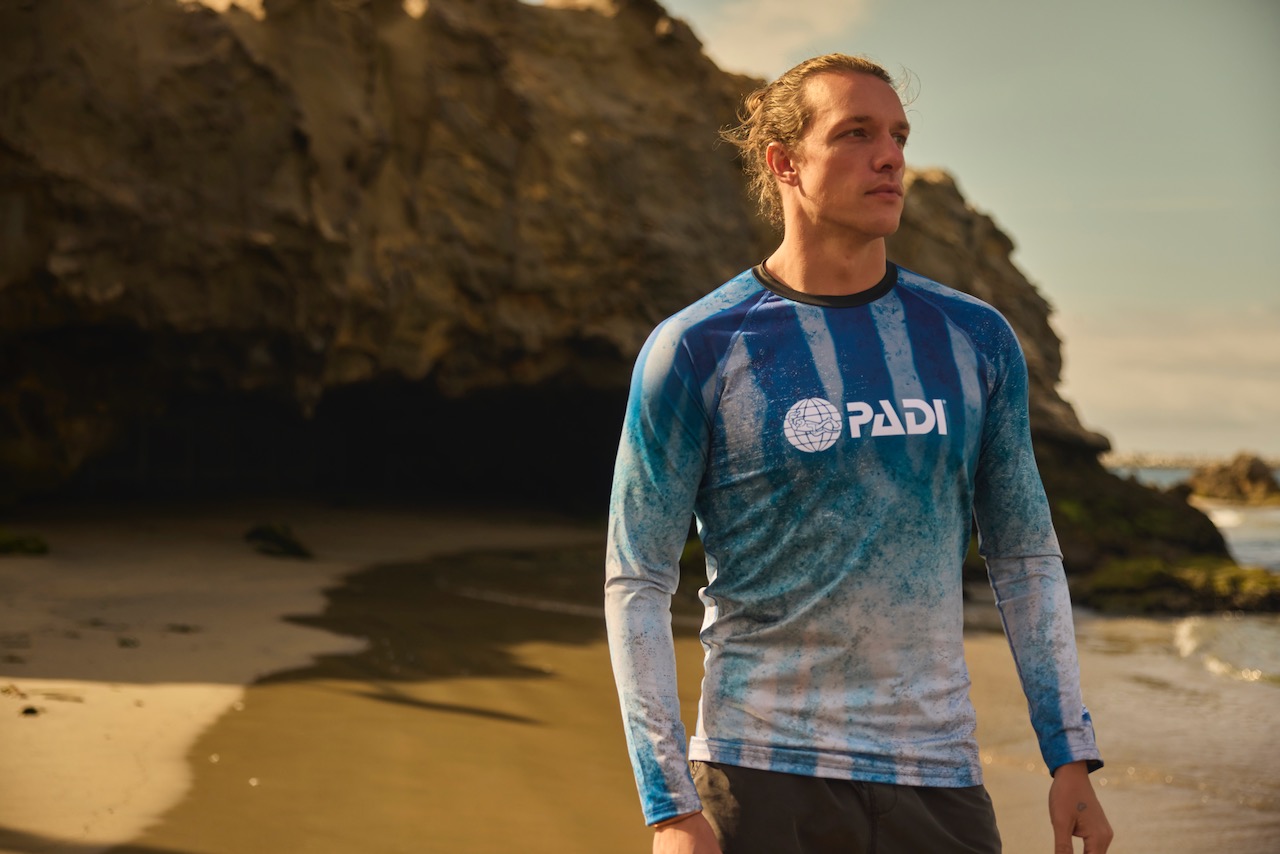 a man stands on the seashore wearing a PADI rashguard