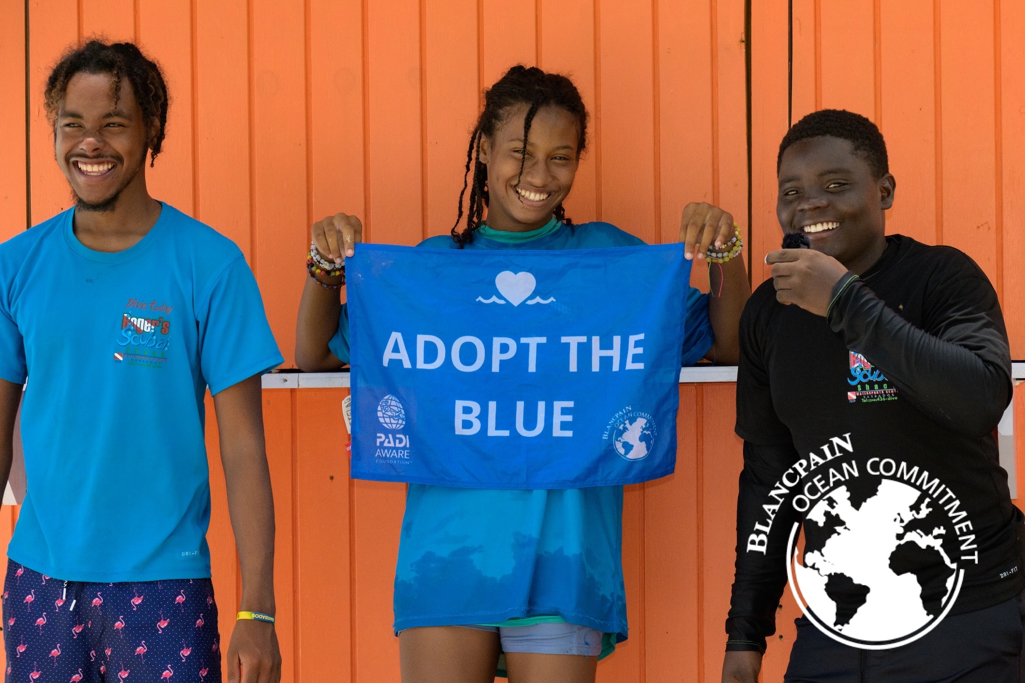 three people stand in front of an orange background and hold an Adopt the Blue flag