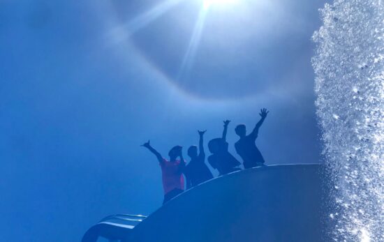 Four people in a boat waving to a photographer in the water.