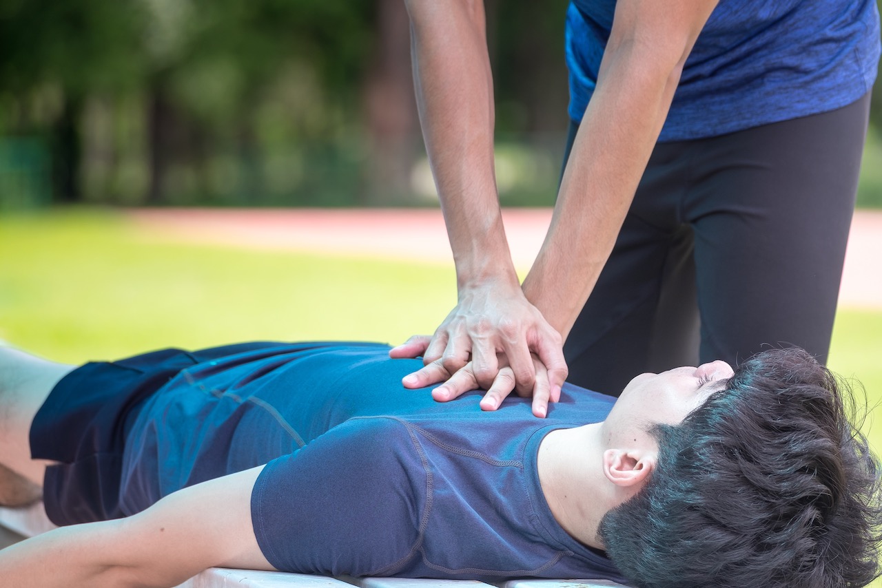 Young athlete making cardiopulmonary resuscitation (CPR) to an unconscious young man after heart attack while exercising at the sports stadium. Concepts of health care, medication and sports.