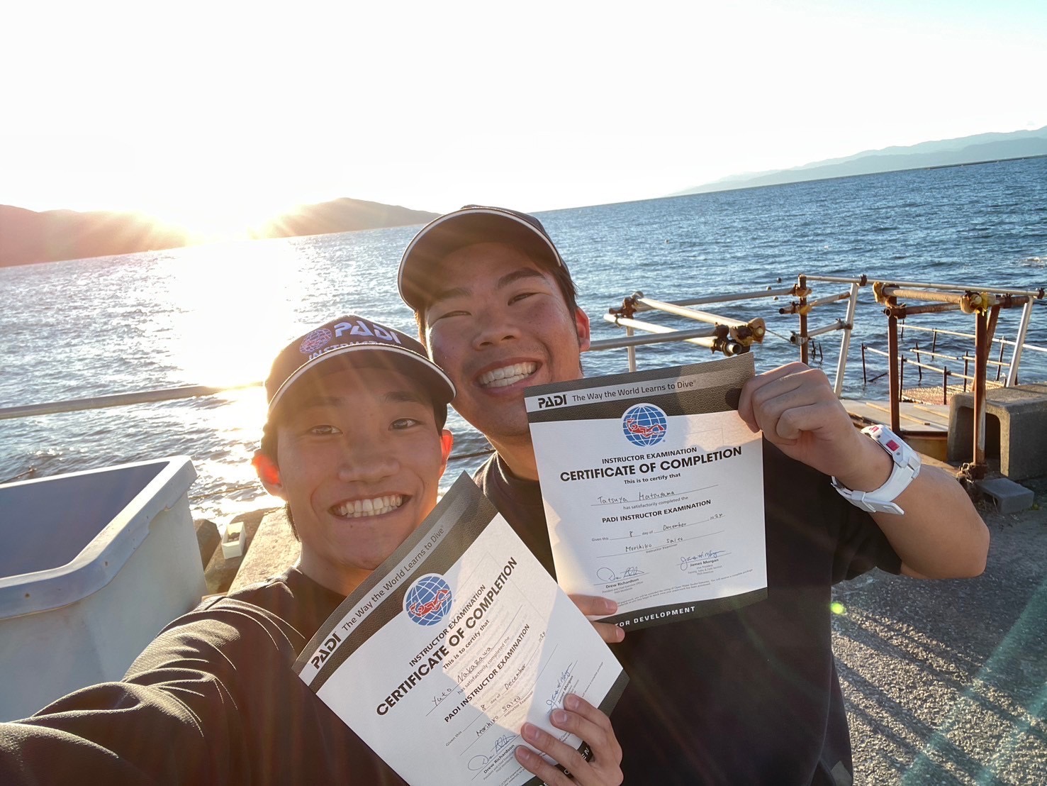 Two young men are newly certified PADI instructors and are holding their certificates happily.