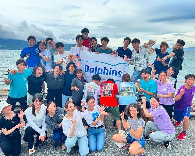 A large group of student divers pose for a group photo with a banner on the bank.