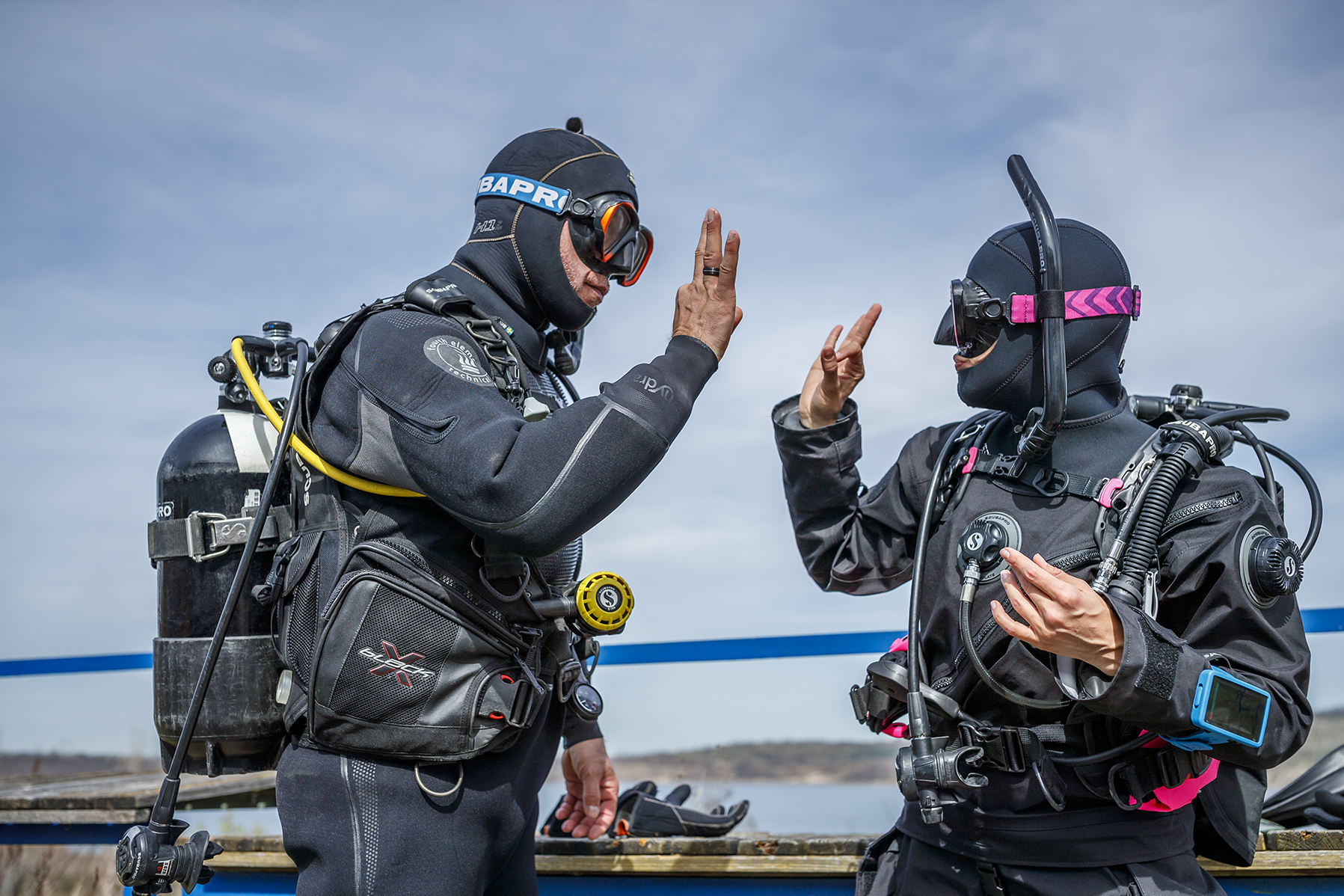 Two scuba divers getting ready for a drysuit dive in front of a lake while showing the ok sign to each other, Geiseltalsee, near Leipzig, Germany, ScubaPro, PADI.