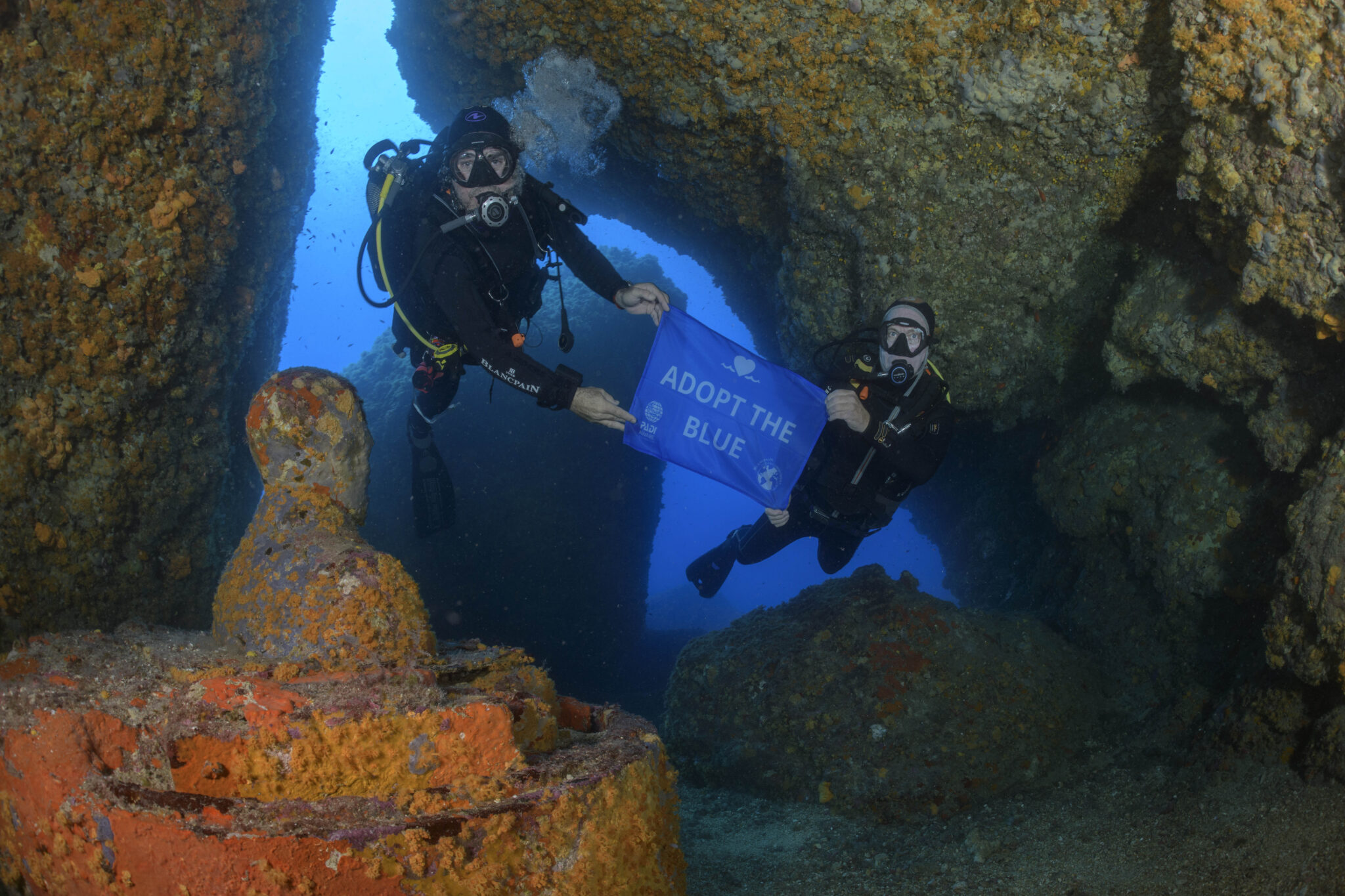 two men scuba dive under some rocks in the ocean