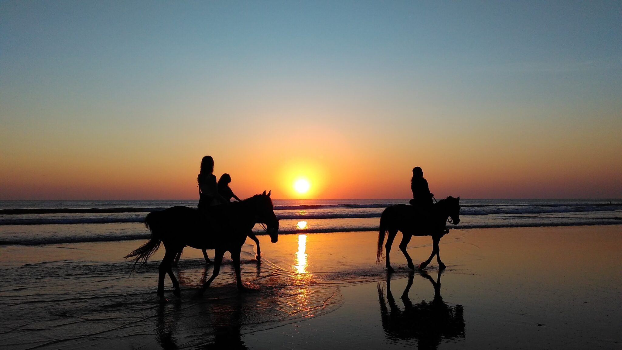 Horseriding at sunset Three horseriders riding along an empty beach at sunset, an extra activity you can enjoy during a scuba vacation in Andalusia