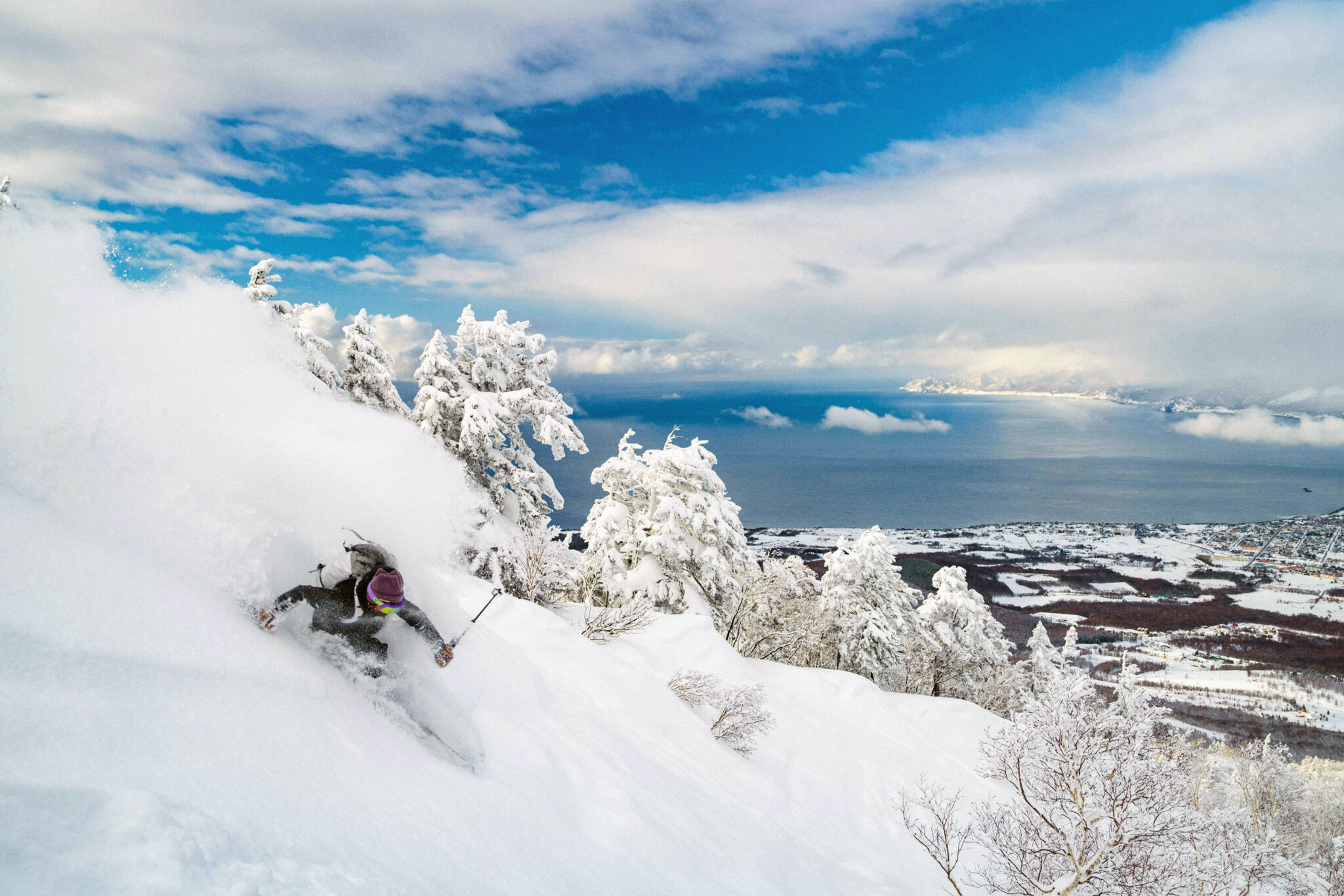 Skiing in Hokkaido, Japan A skier goes down a hill through Japow powder snow with the sea in the background in Hokkaido, which offers skiing and diving