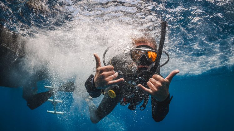 A diver gives two shakas to the camera after jumping into the water