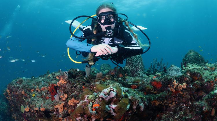 A diver wearing a skeleton rash guard floats facing the camera with her hands folded in front of her