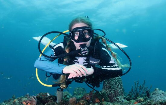 A diver wearing a skeleton rash guard floats facing the camera with her hands folded in front of her
