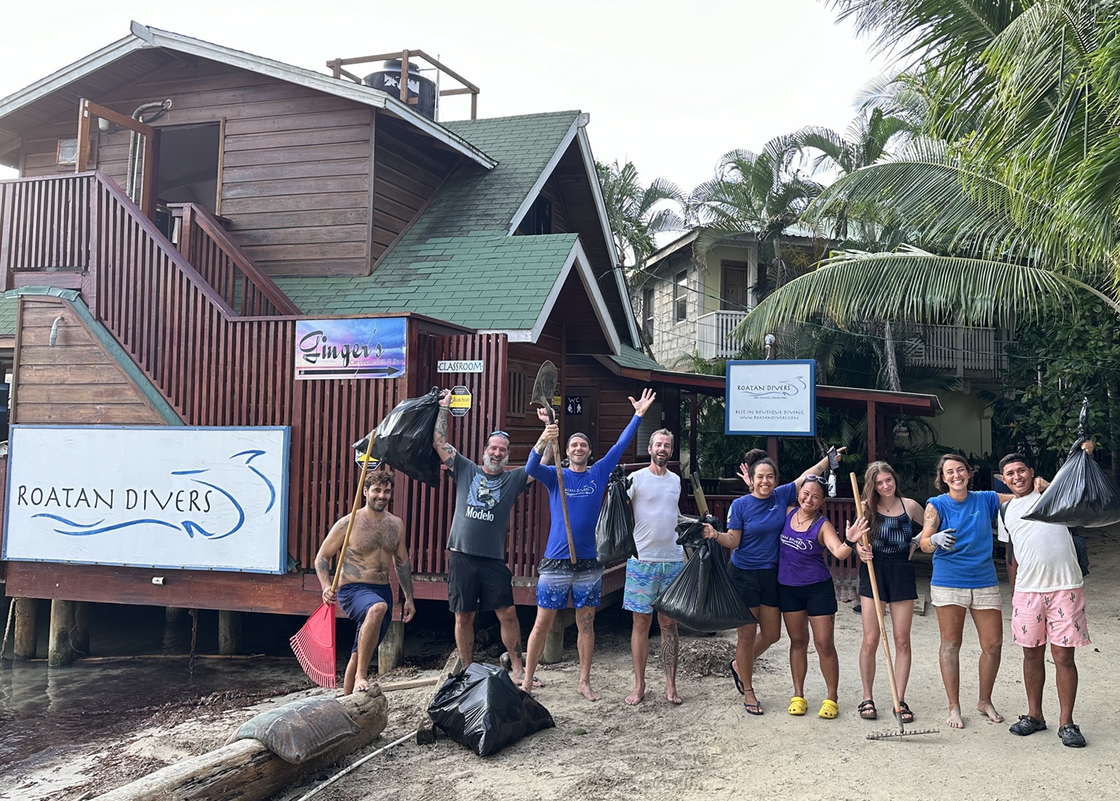 Nine people stand in front of Roatan Divers' building with bags of trash and cleaning tools