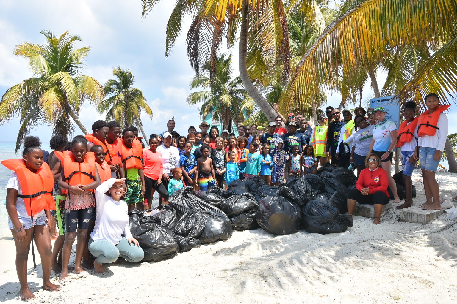 Dozens of volunteers stand behind several bags full of marine debris from a cleanup event
