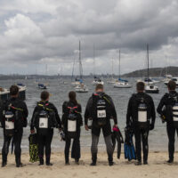 A group of divers preparing for their rescue course stand on shore looking at the water