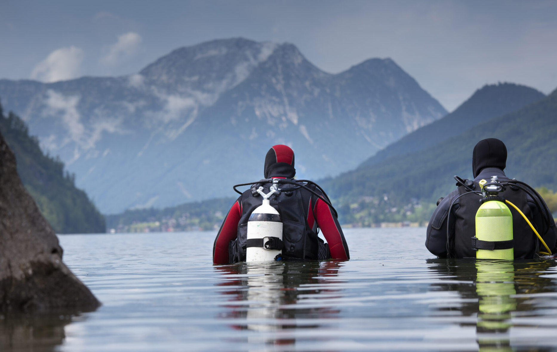A pair of divers admire a scenic mountain backdrop before embarking on a cold water altitude scuba adventure in a Swiss lake