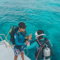 two divers complete buddy checks before diving off the back of a boat