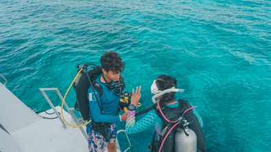 two divers complete buddy checks before diving off the back of a boat
