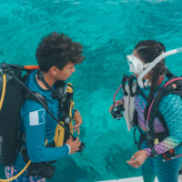 A scuba buddy pair completing pre-dive checks on the boat before their dive